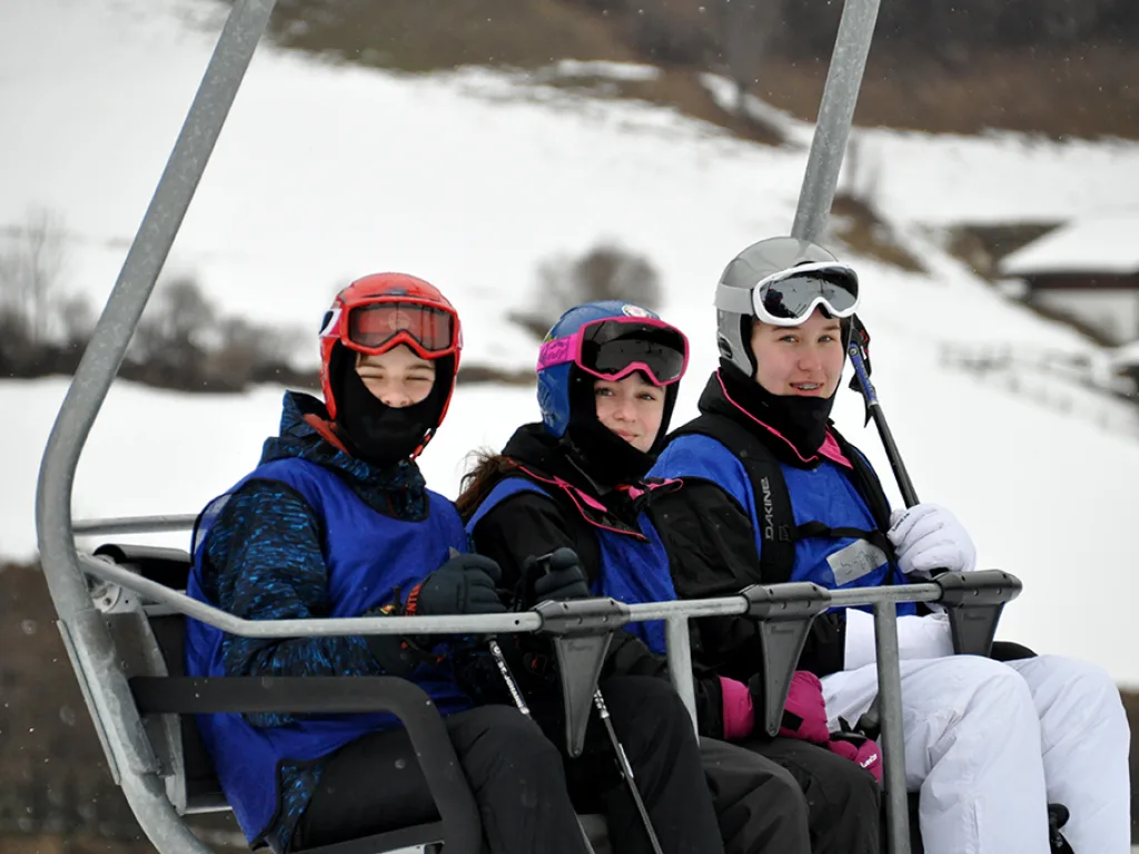Drei Jugendliche mit Helm und Skibrille im Sessellift.